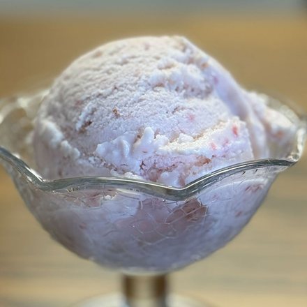 A scoop of homemade strawberry ice cream in a footed glass dish